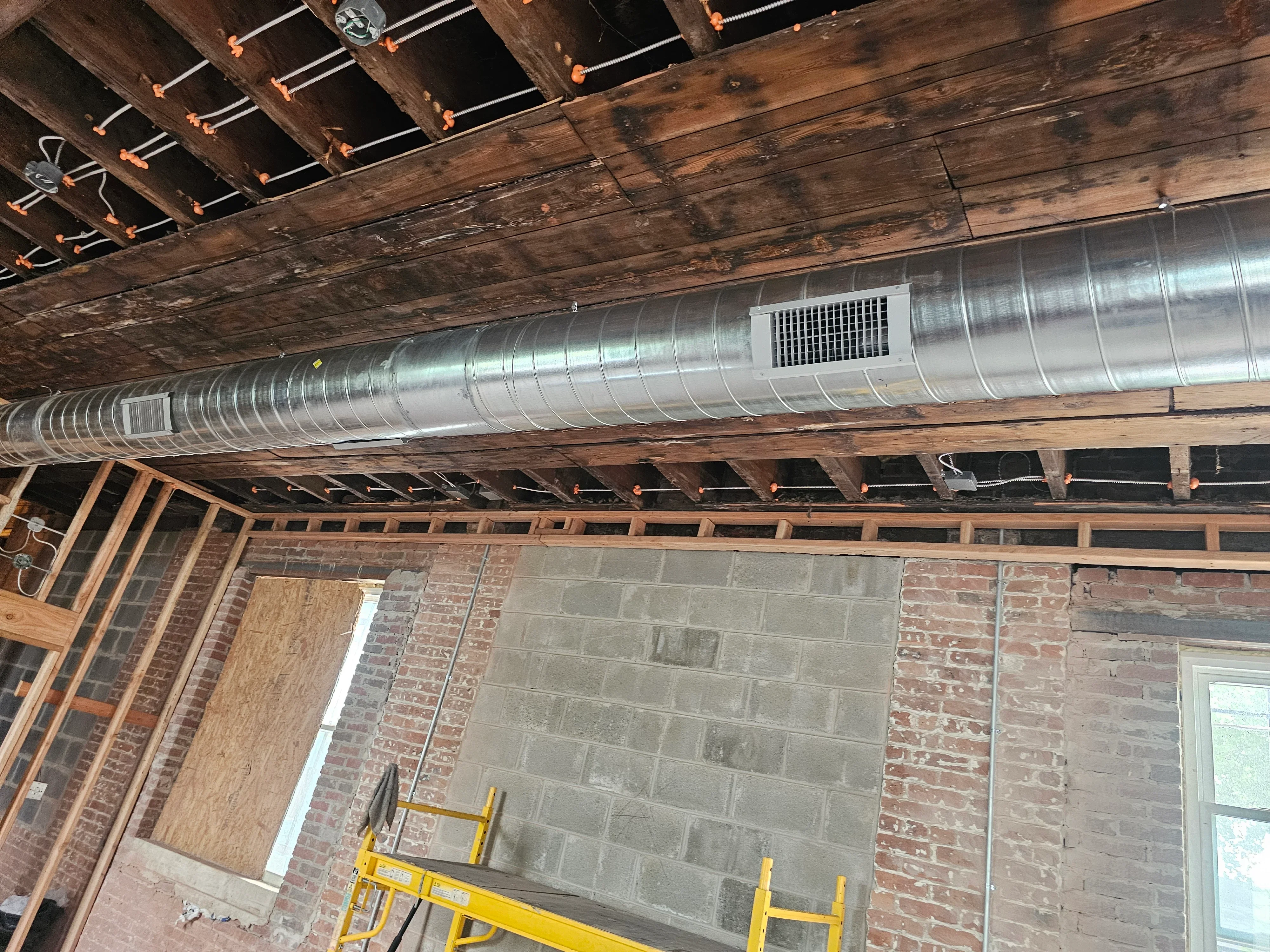 Spiral metal ductwork installed under wooden beams with orange support brackets