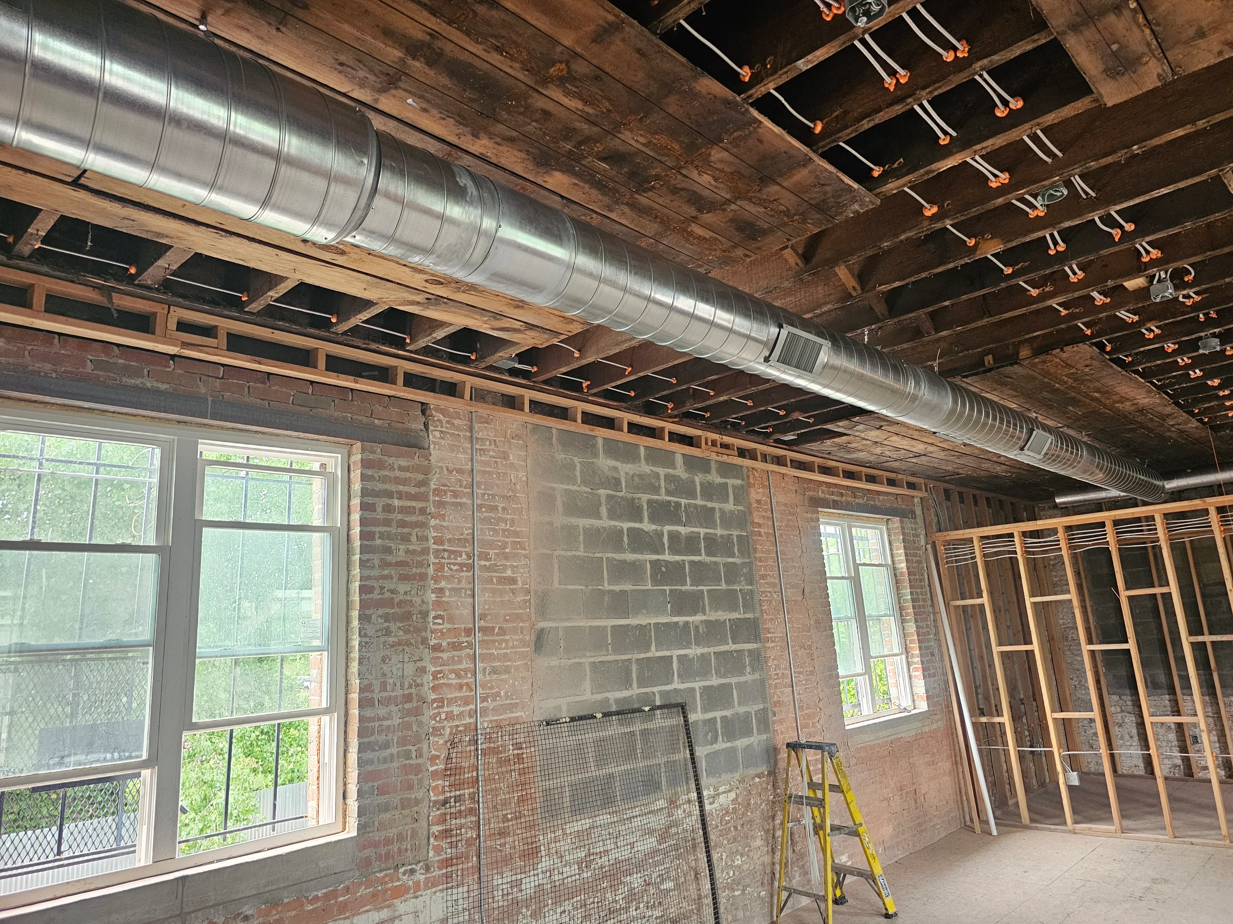 Spiral metal HVAC ducts installed in commercial space with wooden ceiling joists
