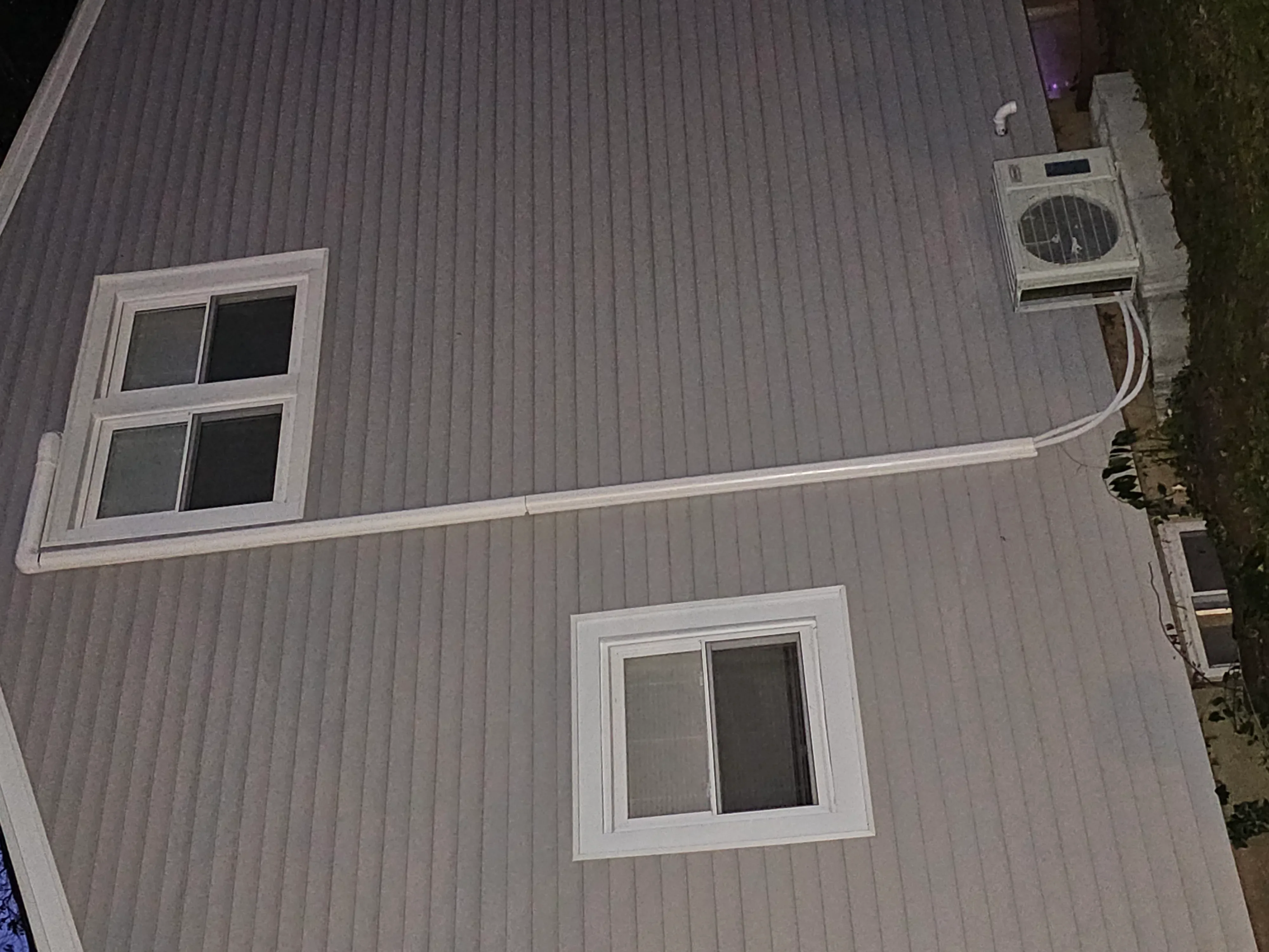 Exterior wall showing installed AC unit with white trim windows and metal siding