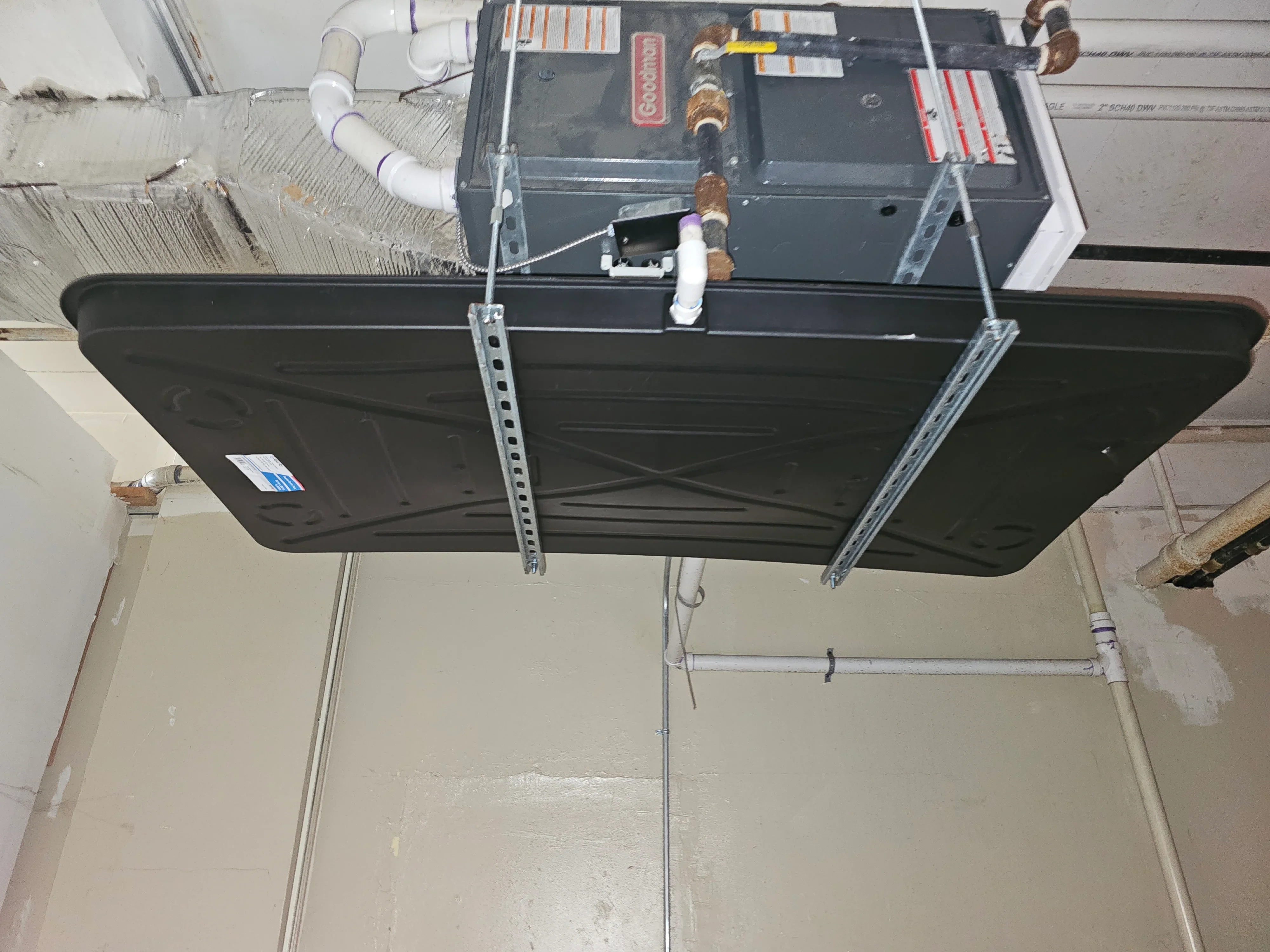 Goodman air handler unit mounted in attic with white PVC ductwork and condensate lines