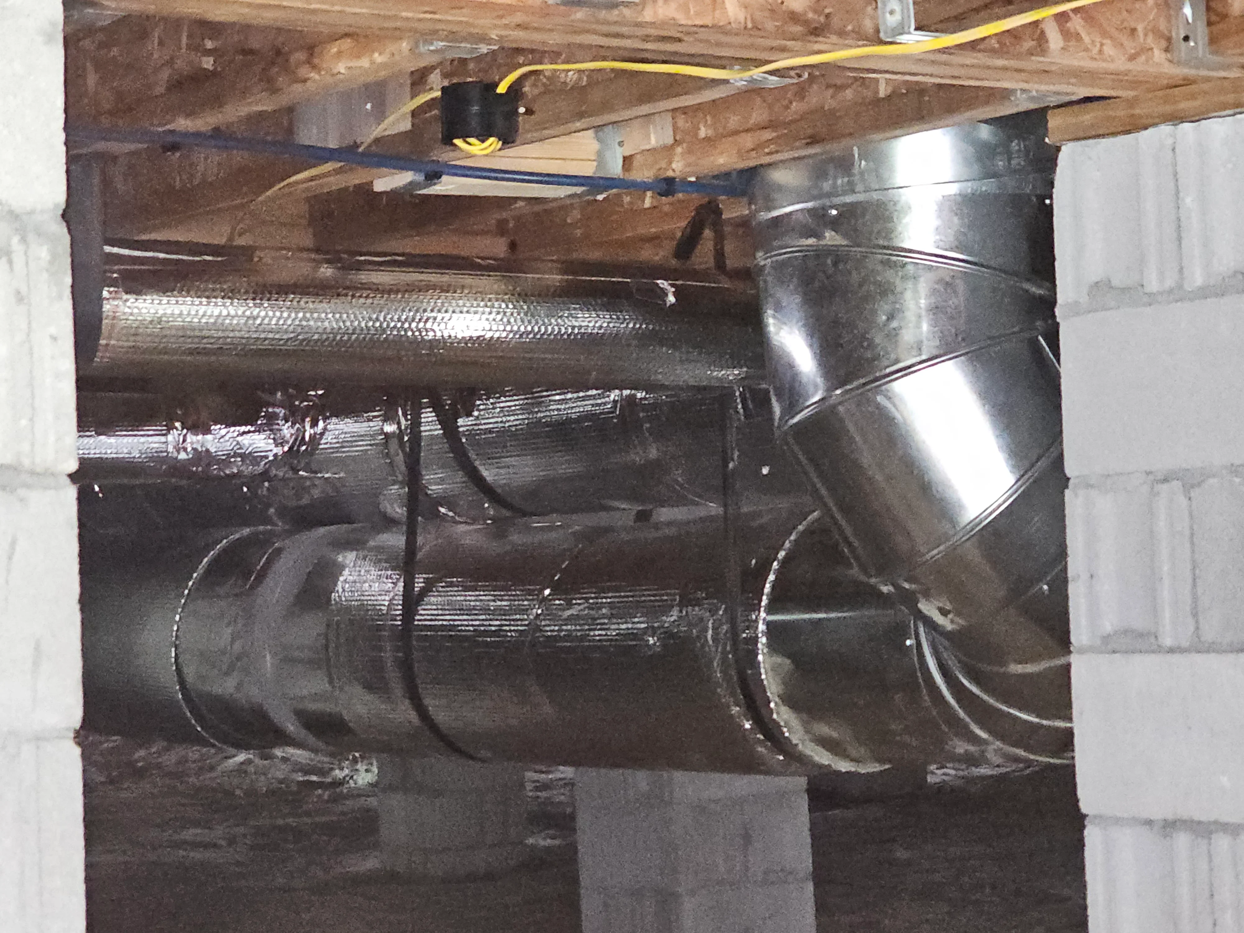 Commercial HVAC ductwork installation with insulated aluminum ducts and electrical wiring mounted to wooden joists