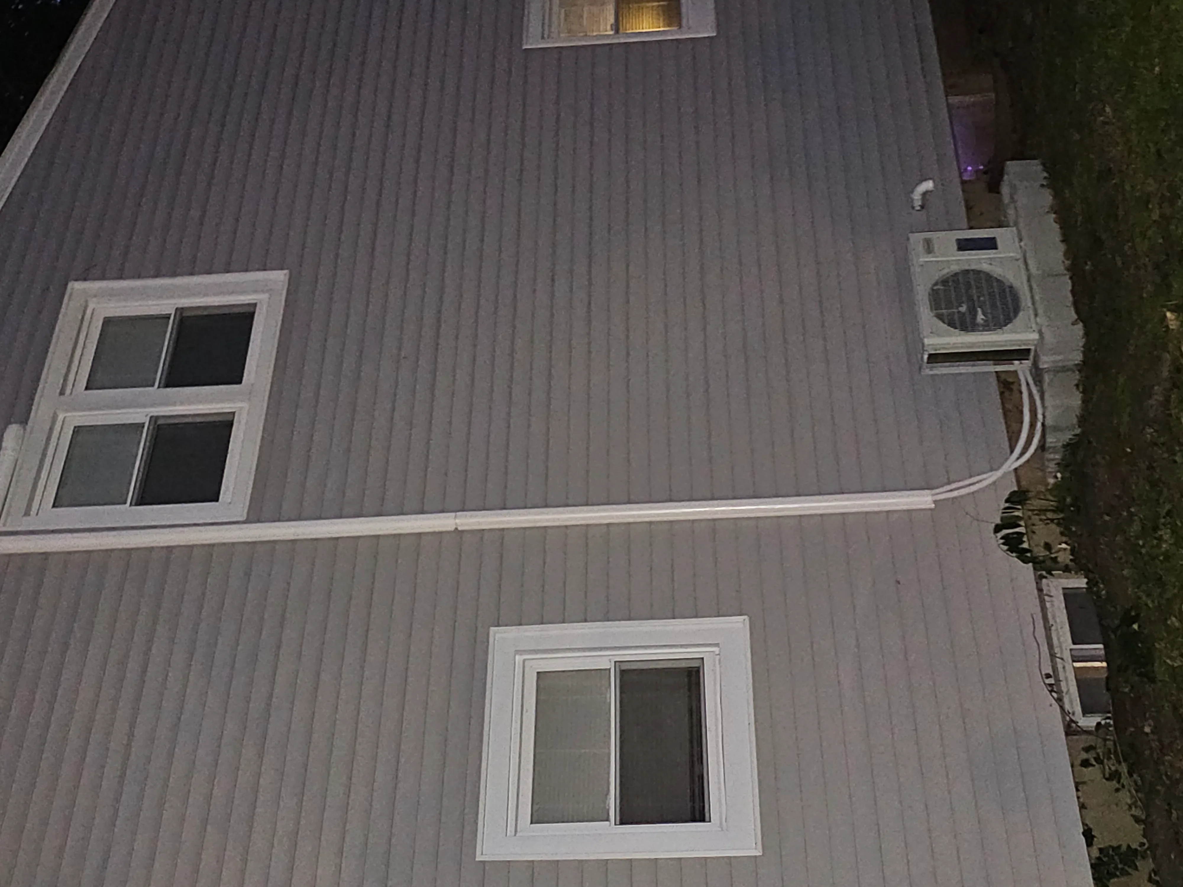 Installed AC condenser unit on residential wall with white trim and corrugated metal siding